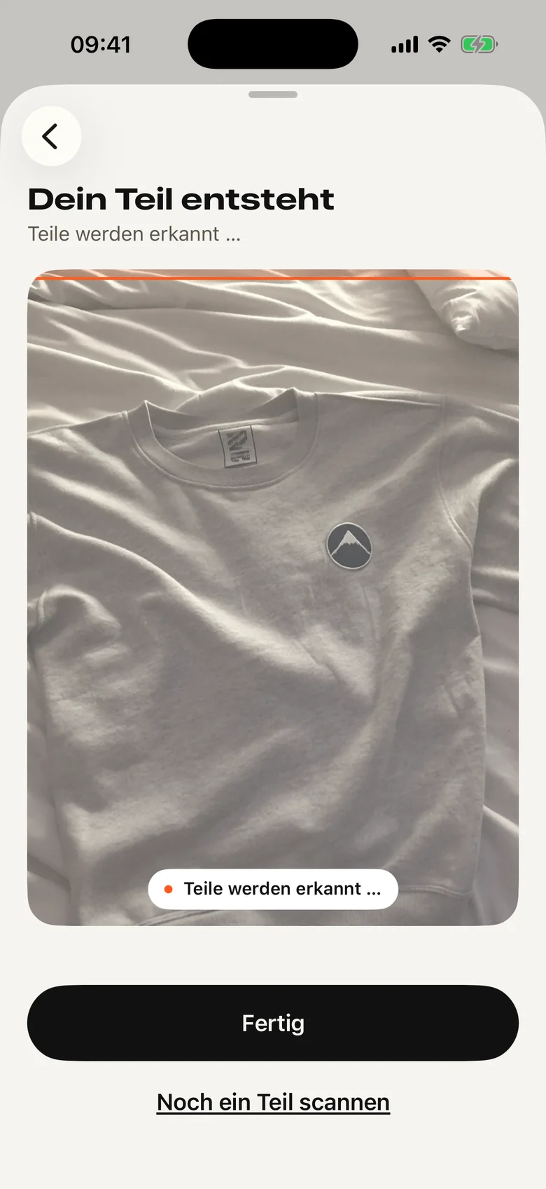 App-Bildschirm „Dein Teil entsteht“: Eine Scanlinie läuft über das Foto eines Sweatshirts, darunter steht „Teile werden erkannt“.