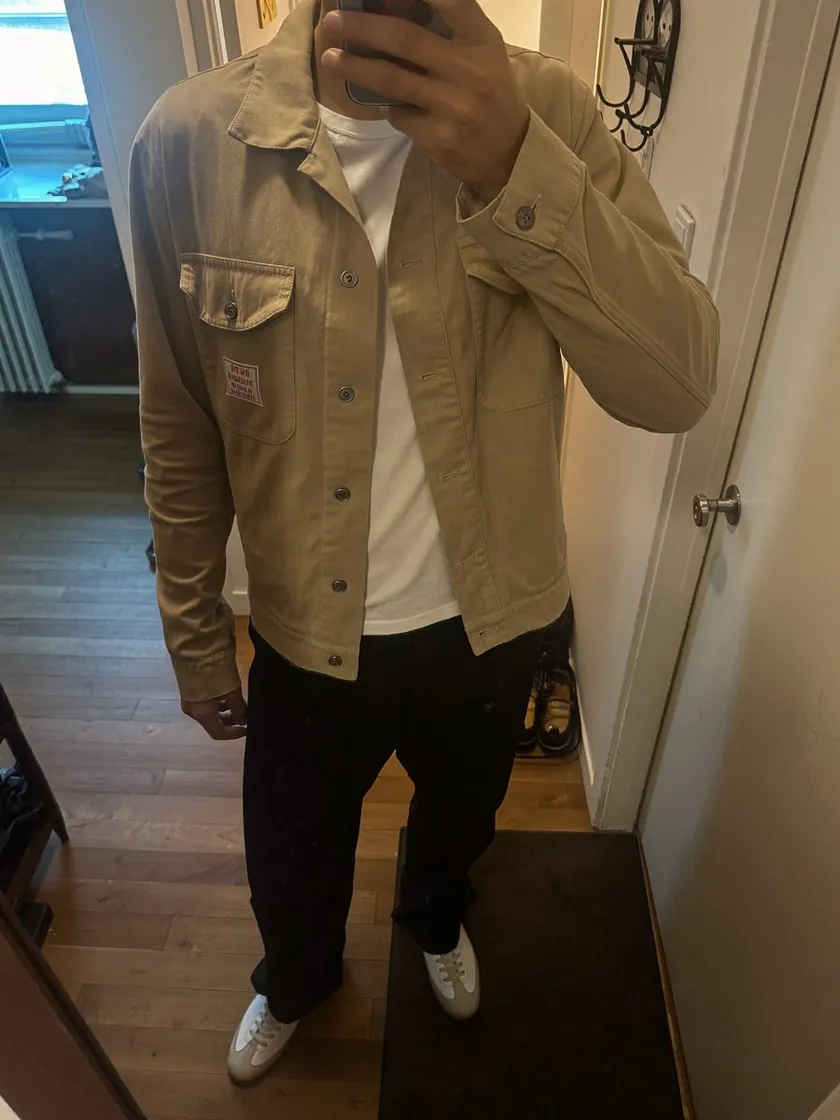 Spiegel-Selfie: eine Person in beiger Hemdjacke, weißem T-Shirt, schwarzer Hose und weißen Sneakern, das Gesicht ist vom Handy verdeckt.